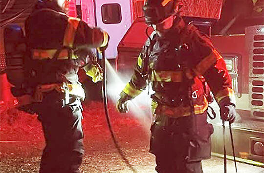 After making short work of a chimney fire NKF&R Lt. Scott Trueblood uses a hose to clean the gear worn by firefighter Tucker Burns. NKF&R Courtesy Photos