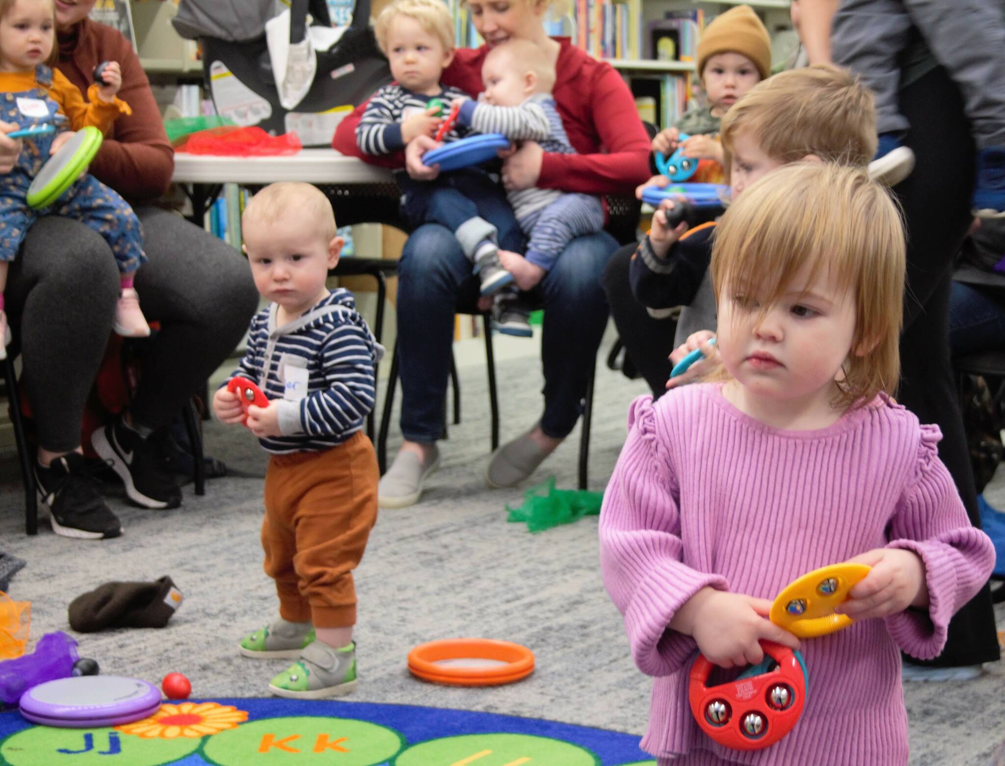 A toddler watches the librarian do actions for a song while catching the eyes of another youngster.