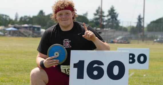 Senior Brendan Bourke claims victory in discus, posing by the 160-foot sign his best throws passed not once but twice. Elisha Meyer/Kitsap News Group Photos