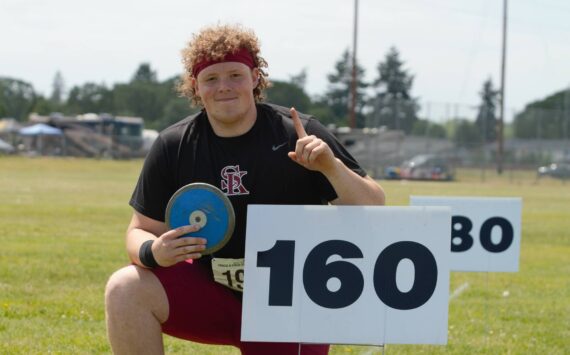 Senior Brendan Bourke claims victory in discus, posing by the 160-foot sign his best throws passed not once but twice. Elisha Meyer/Kitsap News Group Photos