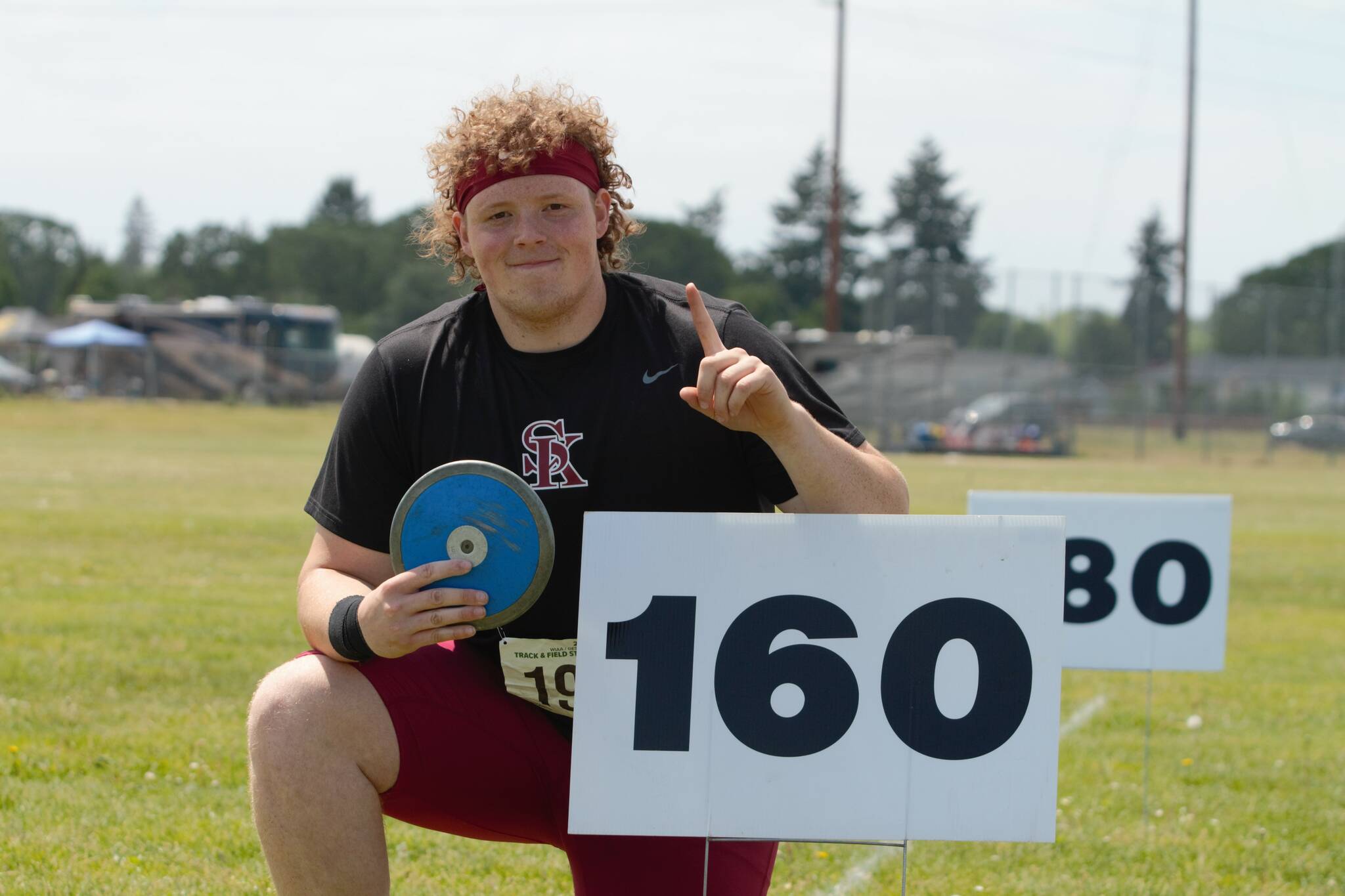 Senior Brendan Bourke claims victory in discus, posing by the 160-foot sign his best throws passed not once but twice. Elisha Meyer/Kitsap News Group Photos