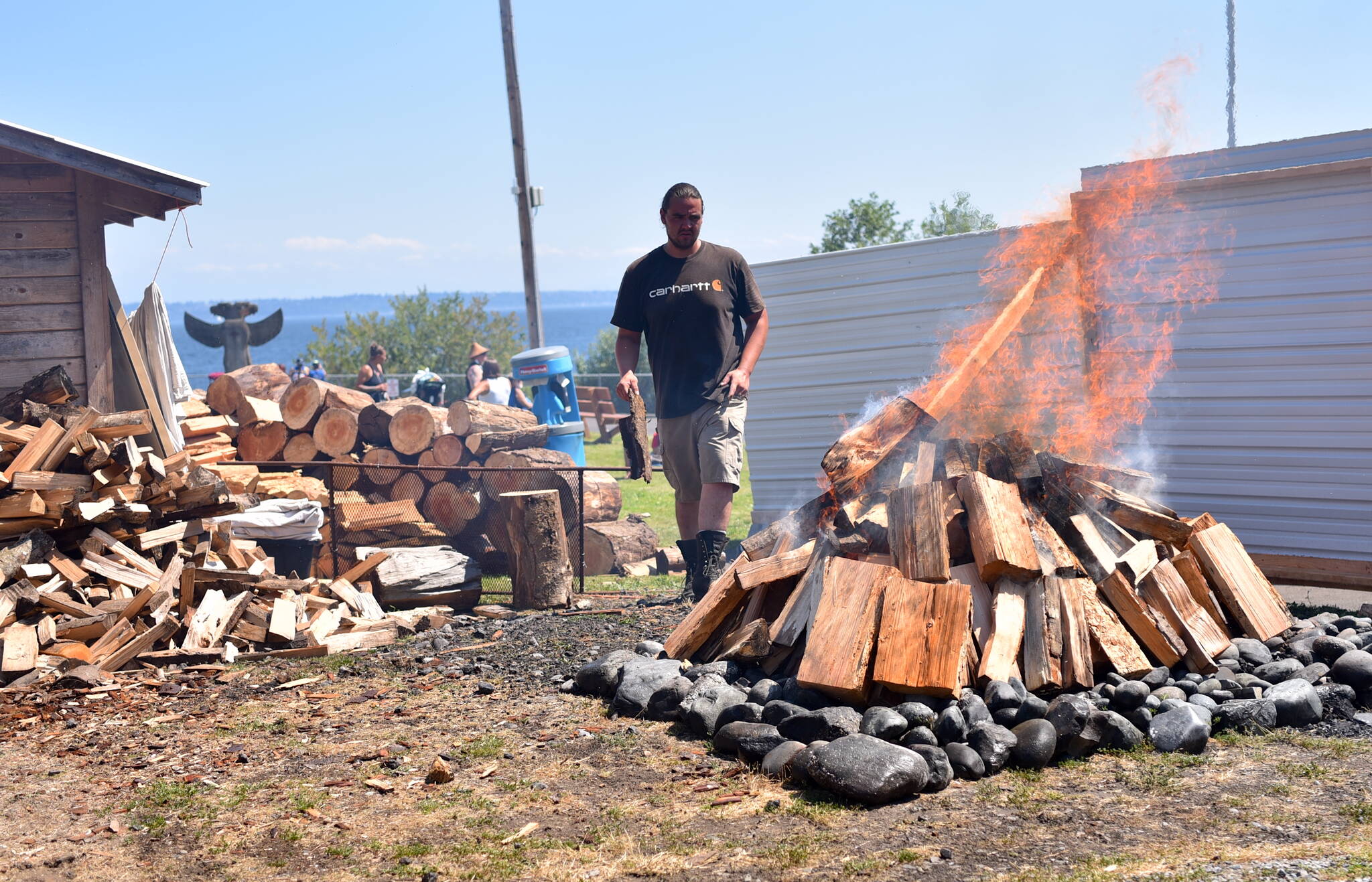 A fire piled high with wood cooks clams for the gathering.