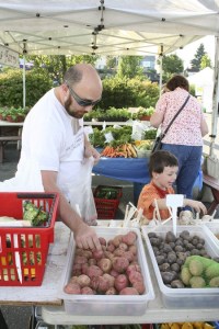 Bremerton resident Adam Metcalf looks over the potatoes Sept. 2 at the Silverdale-based Pheasant Fields Farm stand at the Bremerton Farmers Market with his son