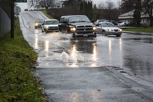 Vehicles traveling down NE Iverson road are cautioned to travel safely and slowly as storm water overflows through man hols and across sections of the road on Jan. 21.