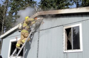 A North Kitsap Fire & Rescue firefighter saws into the attic space of a burning home Thursday off Little Boston Road.