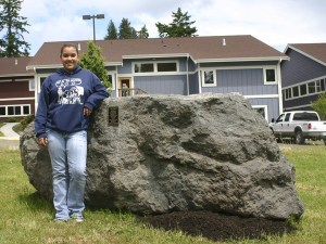 West Sound Academy graduate Liz Leness stands with the 11-ton rock she and her classmates bought and donated to the school. The group of 11 seniors planned to spray paint the rock after their graduation Thursday.