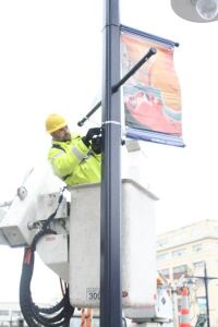 Brian Thompson hangs a banner featuring an image by artist Marlene Dougherty at the intersection of Pacific Avenue and Burwell Street.