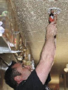 Central Kitsap Fire & Rescue paramedic/firefighter Dan Martin installs a smoke alarm in Abram Rasband’s mobile home at Northlake Mobile Home Park.