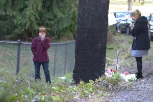 Visitors to the site of the accident pay their respects on Tuesday on NW Finn Hill Road. A memorial at the base of the utility pole continues to grow.