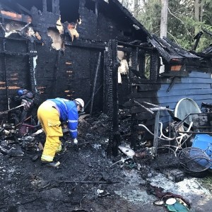 Kitsap County Deputy Fire Marshal Tina Turner sifts through the debris left after a fire swept through a home&rsquo;s attached shed, destroying it and damaging the adjacent structure. Although Turner could not specify the fire&rsquo;s exact cause, officials believe that it began near a space heater and the extension cords supplying it with power. (North Kitsap Fire & Rescue)