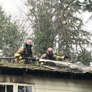 From left, NKF&R Lt. Ryan Buchanan applies water beneath layers of roofing material while Lt. Mark Cooney exposes the hot spots ata Suquamish home fire Jan. 7. (Photo/North Kitsap Fire & Rescue)