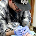 Eric Flint begins tattooing a turtledove on Amber Coe at The Clinic Tattoo on Valentine&rsquo;s Day.                                Michelle Beahm / Kitsap News Group