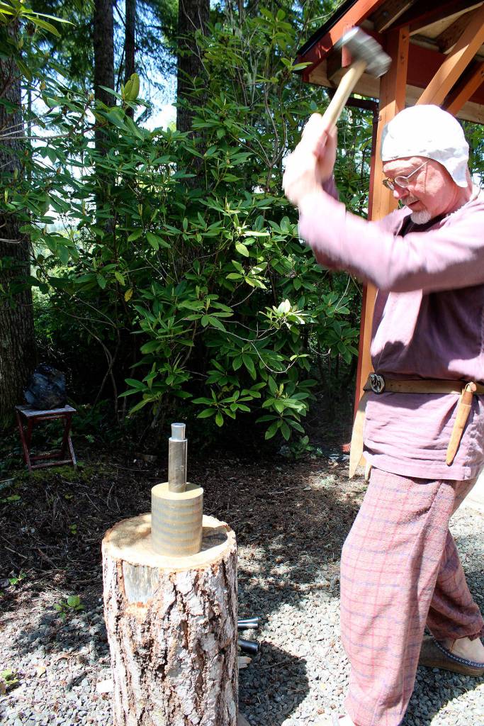 Arion the Wanderer strikes a coin with a six-pound hammer. Normally a second person would be holding the coin dyes he&rsquo;ll strike, with a pewter coin in the middle, but alone Arion utilizes a cylinder that will hold them together instead.                                Michelle Beahm / Kitsap News Group