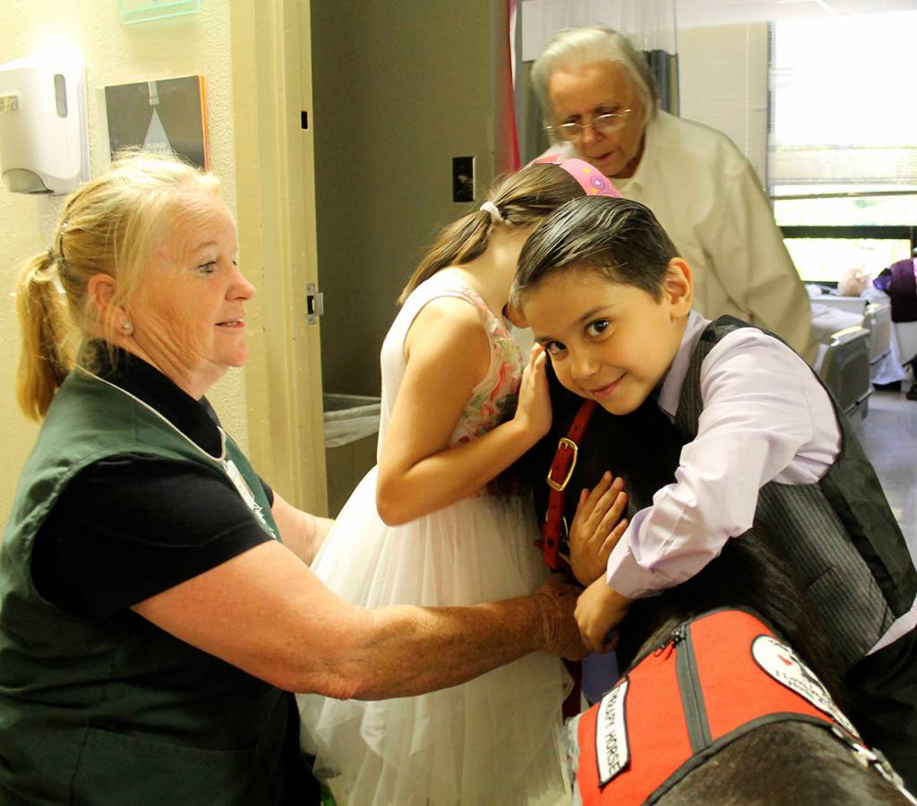 Six year-old Clarence Ulrich and his older sister, Evelyn, hug Diesel while Watland (at left) and the children&rsquo;s great-grandmother watch. It was Evelyn&rsquo;s birthday and Integrative Health Practitioner Evelyn Enns (not pictured) gave both children an official Diesel trading card.                                Terryl Asla/Kitsap News Group