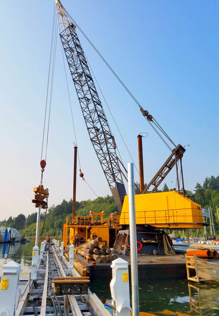 The pile-driving crane places a new galvanized steel piling. The old, creosoted wood pilings the Skookum&rsquo;s crew pulled earlier are stacked on the barge&rsquo;s deck.                                Terryl Asla/Kitsap News Group