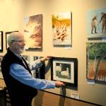 Bill Fulton, current PAL President, lines up fellow artists paintings at Central Market.