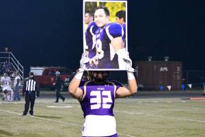 <em>North Kitsaps Dax Solis holds up the picture of teammate Hunter Schaap, who was killed in January, during the coin toss of a playoff game. The team carried his picture with them at every game this season and he remained listed on their official roster. </em>Mark Krulish/Kitsap News Group