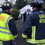 Fire crew members and onlookers were moved away from where an exterior opening was cut into the house so that rescuers could gain better access to the wells location with long ladders. Jeff Faucett, assistant fire chief, said the exterior shingles that were cut likely contained asbestos materials. (Bob Smith | Kitsap Daily News)