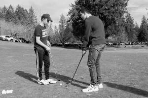 Senior Bryce Kahle, left, helps freshman Mathew Quall during practice at Gold Mountain Golf Course on March 12. (Jacob Moore/Kitsap News Group)