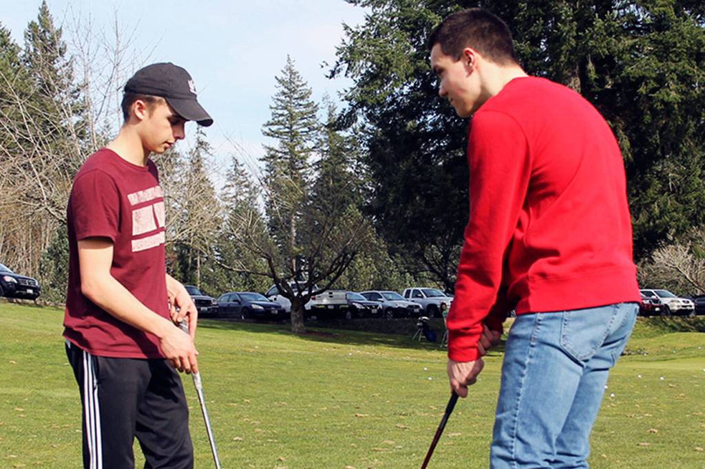 Senior Bryce Kahle, left, helps freshman Mathew Quall during practice at Gold Mountain Golf Course on March 12. (Jacob Moore/Kitsap News Group)
