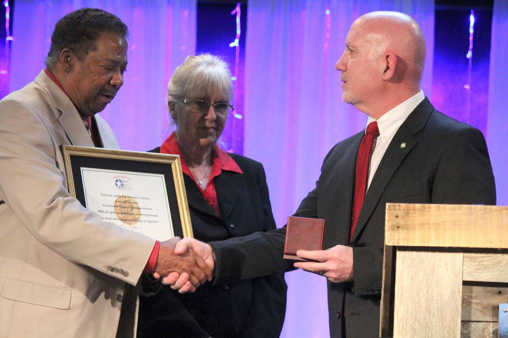 <em>Robert and Carolynn Perkins accept a replica of the Congressional Gold Medal on behalf of Roberts father, Roscoe Perkins.</em>                                Michelle Beahm/Kitsap News Group                                Robert Perkins accepts the congratulations of friends and family after accepting the Congressional Gold Medal on behalf of his late father, Roscoe C. Perkins.                                Michelle Beahm | Kitsap News Group