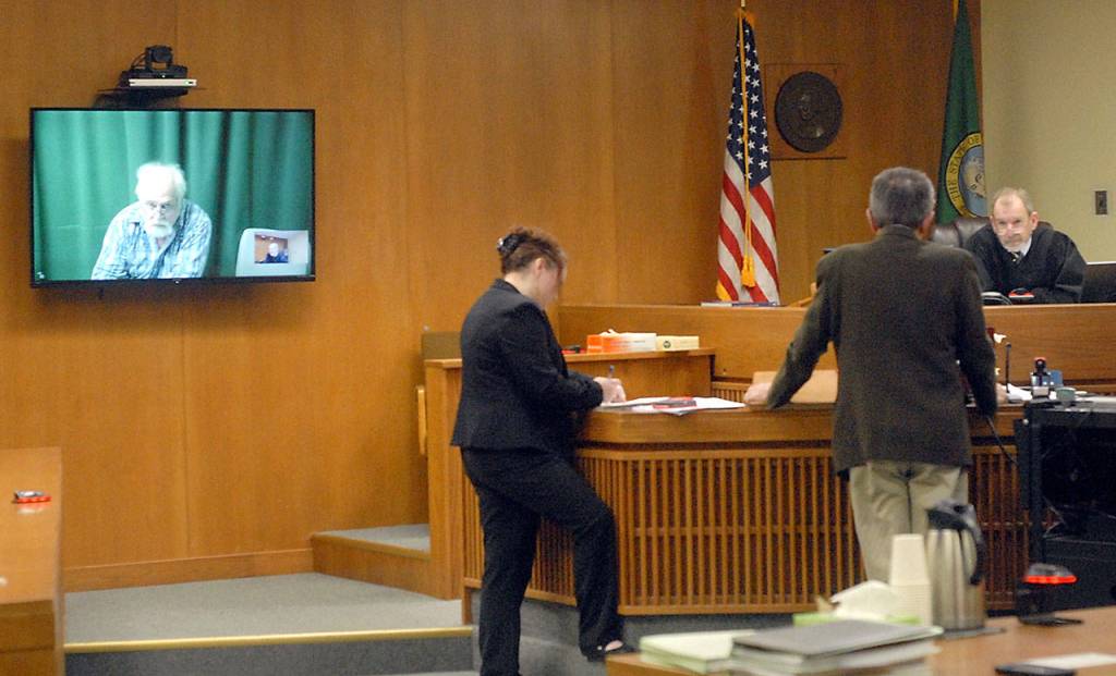 Clinton R. Caldwell, 67, of Sequim appears on a television monitor in Clallam County Superior Court on Tuesday as Chief Criminal Deputy Prosecuting Attorney Michele Devlin and attorney John Hayden stand before Superior Court Judge Chris Melly in Port Angeles. (Keith Thorpe/Peninsula Daily News)