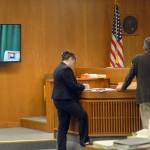 Clinton R. Caldwell, 67, of Sequim appears on a television monitor in Clallam County Superior Court on Tuesday as Chief Criminal Deputy Prosecuting Attorney Michele Devlin and attorney John Hayden stand before Superior Court Judge Chris Melly in Port Angeles. (Keith Thorpe/Peninsula Daily News)
