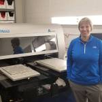 Alisha Weiss stands beside Skyhawk Press Kornit direct to garment printer. Nick Twietmeyer | Kitsap News Group.