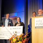 Meg Depew (center) of Sequim Bee Farm of Port Angeles accepts the grand prize of $20,000 in the annual edg3 FUND small business competition at a ceremony in Bremerton. Co-owner Buddy Depew is at the podium. At each end is Tony George (left), Kitsap Bank president and COO, and Steve Politakis, Kitsap Bank CEO. The competition was sponsored by Kitsap Bank. (Kitsap Bank photo)