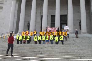 Seattle Public Schools librarians hold up signs on the capitol building steps, in protest of funding cuts that have resulted in cuts to libraries. Kate Eads, who organized the event, can be seen holding a megaphone addressing the group.Photo by Emma Epperly, WNPA Olympia News Bureau