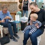 Silhouette artist Karl Johnson creates a portrait of 11-month-old Gabriel Miller, who sits in the lap of his mother, Carly. (Bob Smith | Kitsap Daily News)