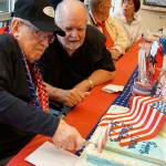 Stanley Hansen slices the first piece of cake at his 100th birthday celebration at the Washington Veterans Home in Retsil on May 24. Hansens son, Don Hansen of Tenino, sits next to the birthday boy. (Bob Smith | Kitsap Daily News)