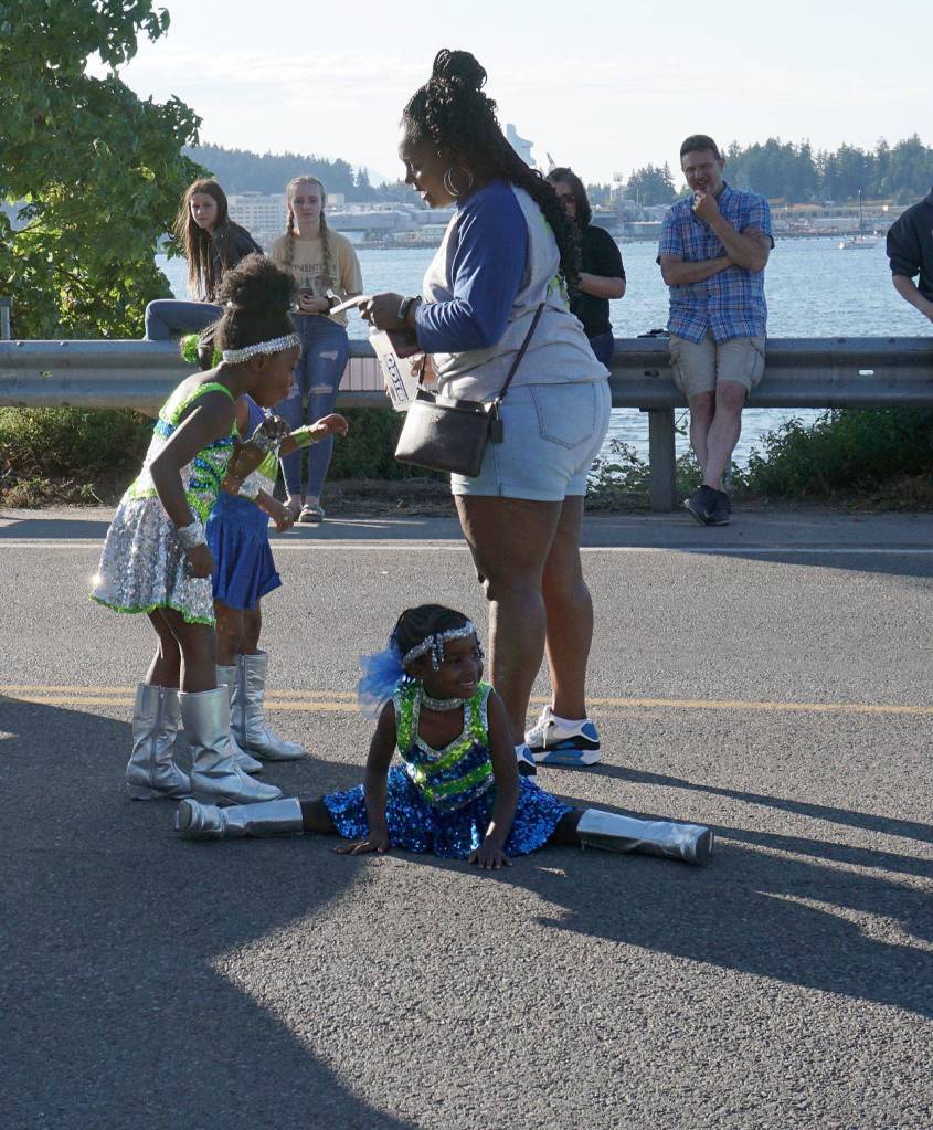 A little member of the Washington Diamonds Drill Team and Drumline takes a rest on the pavement during a pause in the Fathoms parade. (Bob Smith | Kitsap Daily News)