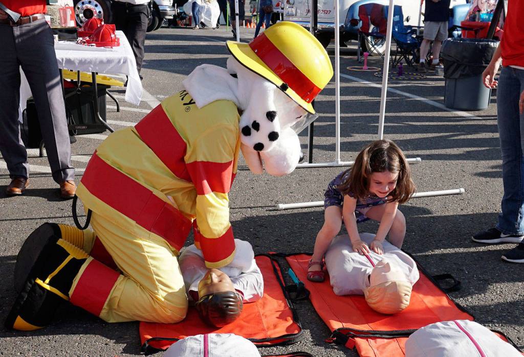 A youngster competes with Sparky to restart the heart of a CPR practice manikin. (Bob Smith | Kitsap Daily News)