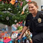 Amy Coull, the Port Orchard Police Departments public safety officer, kneels next to a large assortment of new toys and gifts as part of the departments Giving Tree program with the South Kitsap Helpline organization. (Bob Smith | Kitsap Daily News)