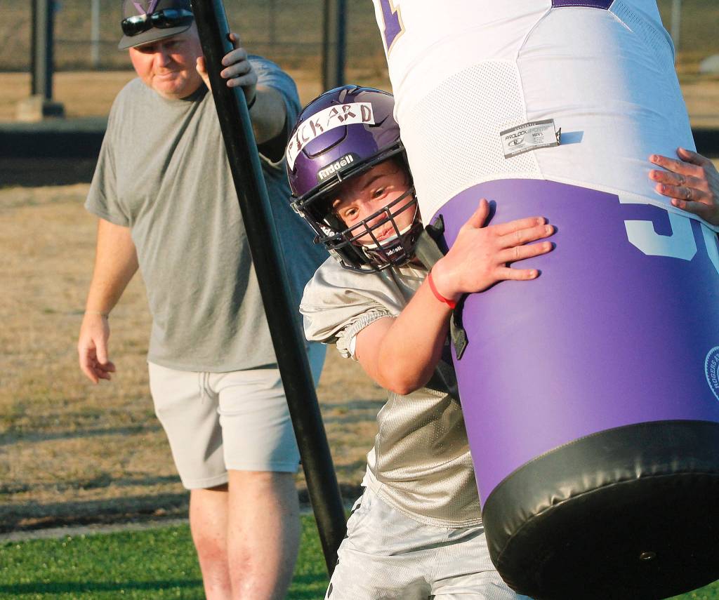 Sophomore Kaden Pickard takes on the tackling dummy as head coach Jeff Weible looks on during practice. (Mark Krulish/Kitsap News Group)
