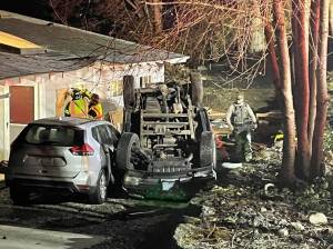 Firefighters work to board up a broken window while a sheriffs deputy investigates the scene after a pickup came off of West Kingston Road, injuring its driver and causing significant damage to a home and an adjacent parked car Nov. 10. Courtesy Photo