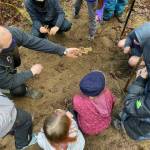 A teacher works with students in the dirt.