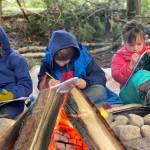 Students write in journals around a campfire at WildWise School. Courtesy Photos