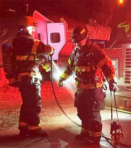 After making short work of a chimney fire NKF&R Lt. Scott Trueblood uses a hose to clean the gear worn by firefighter Tucker Burns. NKF&R Courtesy Photos