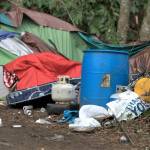 Piles of trash sit between various tarps and tents in the homeless encampment.