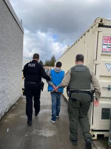 The 30-year-old suspect is led away still wearing a work uniform by law enforcement. Courtesy Photo