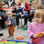 A toddler watches the librarian do actions for a song while catching the eyes of another youngster.