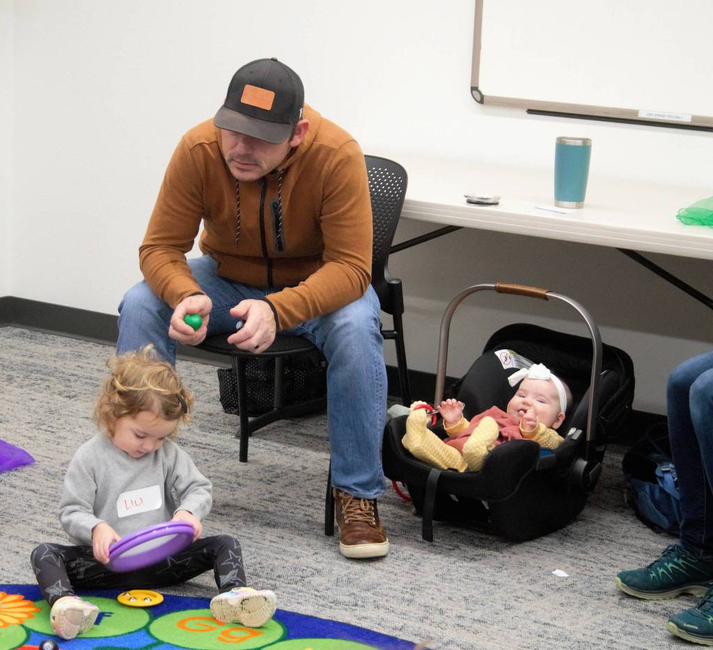 Dad watches his kid play with a drum pad. Even the child in the car seat is enjoying the performance.