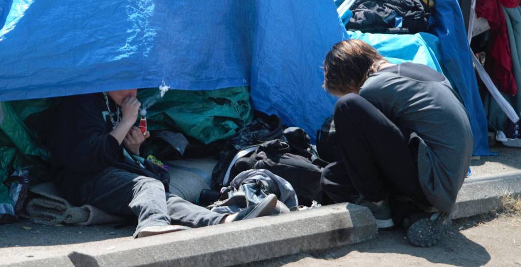 A resident of the encampment smokes a controlled substance out of a pipe.