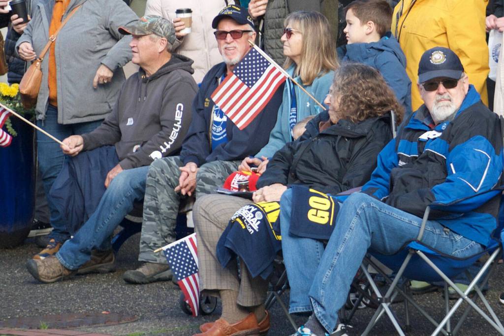 Community members, wearing military apparel and waving American flags, wait for the parade to get started.