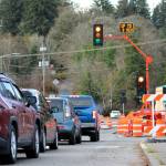 Cars line up behind a lengthy red light for their turn to drive through the active construction zone. The sign informs drivers that the next green may take up to three minutes.