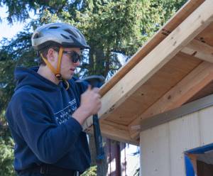 Student James Phillips secures a piece of plywood to the roof of the Hyla students tiny home project.