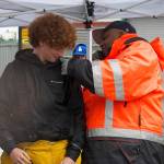 Boatswain Derrick Fant assists student Jack Carrieds don firefighting gear in a demonstration.