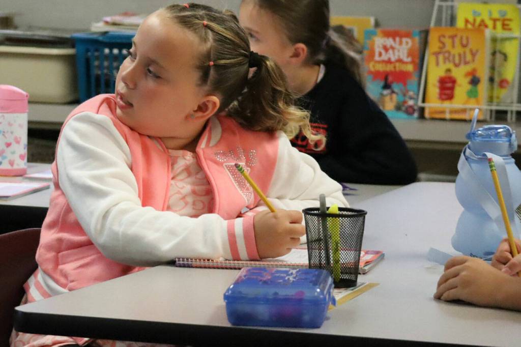 A student turns her head toward the front of the class while writing down notes.